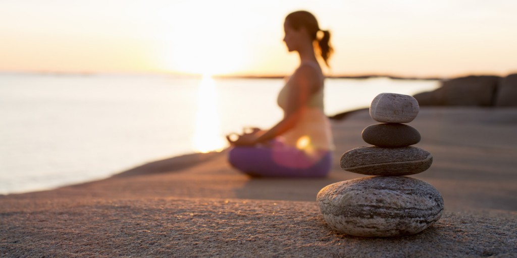 Side view of woman sitting in lotus position on lakeshore with focus on stack of stones