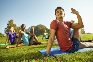 Young man stretching in a outdoor yoga class with others in the background